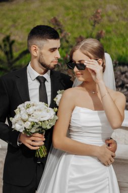 Gelin ve damat resim için poz veriyor, gelin beyaz bir elbise ve damat takım elbise giyiyor.