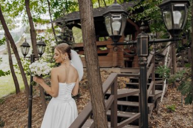 Bir gelin elinde bir buket çiçekle ahşap bir merdivenden iniyor. Sahne, etrafı ağaçlarla çevrili bir ormanda geçiyor. Gelin beyaz bir elbise ve duvak takıyor.