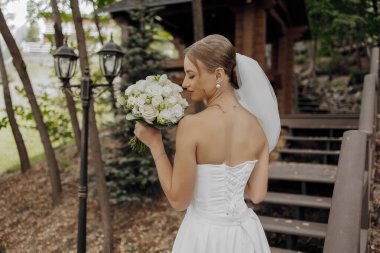 Elinde bir buket çiçek tutan beyaz elbiseli bir kadın. Kadın büyük ihtimalle bir düğüne ya da özel bir etkinliğe katıldığı için zarafet ve kutlama kavramı.