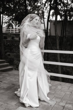 Gelinlikli bir kadın çitin önünde duruyor. Duvak ve beyaz bir elbise giyiyor.