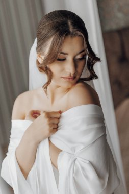 Beyaz bir elbise ve duvak takan bir kadın var. Elinde kırmızı bir nesne tutuyor.