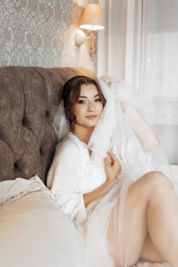 Kafasında beyaz bir peçe olan bir kadın yatakta oturuyor. Beyaz bir elbise giyiyor ve düğüne hazırlanıyor.