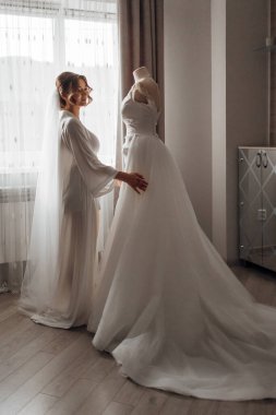 Bir gelin ve nedimesi gelinliğin önünde dikiliyorlar.