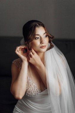 Bir kadın düğüne hazırlanıyor. Beyaz bir elbise ve duvak takıyor. Küpelerini takıyor ve saçını düzeltiyor.