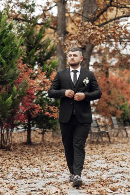 Takım elbiseli ve kravatlı bir adam elinde bir buket çiçekle parkta yürüyor.