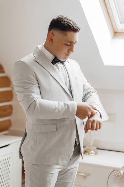 Takım elbiseli bir adam siyah papyon takıyor ve saatini kontrol ediyor. Resmin profesyonel ve resmi bir havası var. Takım elbiseli ve kravatlı bir adam.