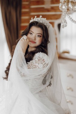 Duvağı ve tacı olan beyaz elbiseli bir kadın. Bir resim için poz veriyor.