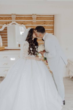 Gelin ve damat aynanın önünde öpüşürler. Gelin beyaz bir elbise giyiyor ve damat beyaz bir takım elbise giyiyor.