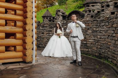 Gelin ve damat bir şatonun önünde, gelin bir buket çiçek tutarken. Sahne romantik ve resimli. Kale, çiftin özel günü için güzel bir zemin görevi görüyor.