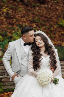 Gelin ve damat resim için poz veriyor, gelin beyaz bir elbise ve damat takım elbise giyiyor.