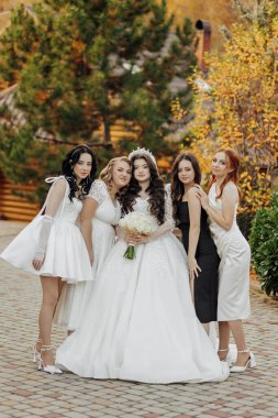 Bir grup kadın bir fotoğraf için poz veriyor, içlerinden biri beyaz bir gelinlik giyiyor.