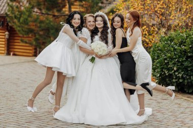 Bir grup kadın bir fotoğraf için poz veriyor, içlerinden biri gelinlik giyiyor. Gelin bir buket tutuyor, ve diğer kadınlar etrafında dikiliyor, gülümsüyor ve kameraya poz veriyorlar.