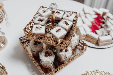 İçinde kekler ve kekler de dahil olmak üzere çeşitli tatlılar barındıran altın tepsili bir masa. Tatlılar onları çekici ve davetkar gösterecek şekilde düzenlenmiş. Masa kurulumu sıcak bir ortam yaratır.