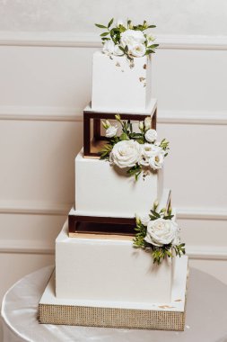 Beyaz çiçekli ve altın aksanlı dört katlı bir düğün pastası. Pasta bir masaya konur ve odanın en önemli parçasıdır.