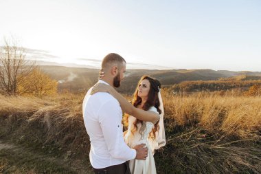 Bir adam ve bir kadın, bir tarlada durmuş kadına sarılıyorlar. Sahne romantik ve samimi.