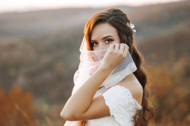 Bir kadın peçe takıyor ve tarlada duruyor. Yüzünde bir gülümsemeyle kameraya bakıyor.