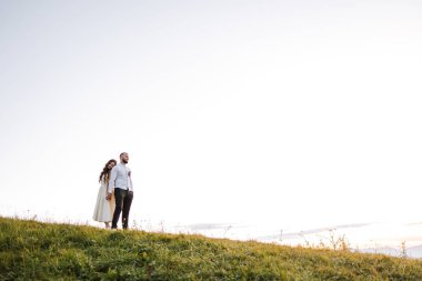 Bir çift tepenin yamacında durmuş, ufka bakıyorlardı. Gökyüzü açık ve güneş parlıyor.