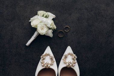 İnci süslemeli ve yaka çiçekli bir çift beyaz ayakkabı. Ayakkabılar karanlık bir yüzeye yerleştirilir ve yaka çiçeği onların yanındadır. Zarafet ve incelik kavramı
