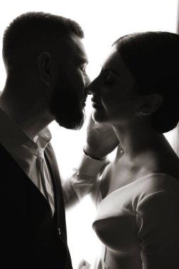 Bir erkek ve bir kadın öpüşüyorlar. Adam takım elbise giyiyor ve kadın da gelinlik giyiyor. Sahne romantik ve samimi.