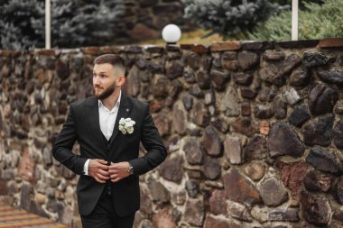 Takım elbiseli bir adam taş bir duvardan aşağı yürüyor. Elinde bir çiçek tutuyor.