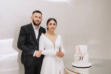 Bir adam ve bir kadın düğün pastasının önünde üzerinde H harfi olan bir resim için poz veriyorlar.