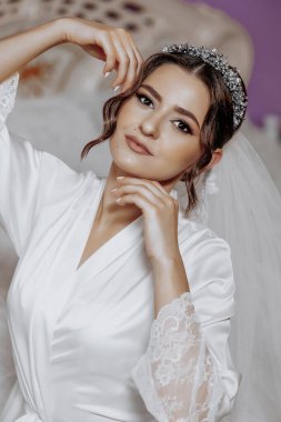 Beyaz bornoz ve duvak takan bir kadın var. Gülümsüyor ve kameraya bakıyor.