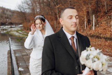 Gelin ve damat, gelin beyaz kürk manto ve damat siyah takım elbise giyerek köprüde dururlar.