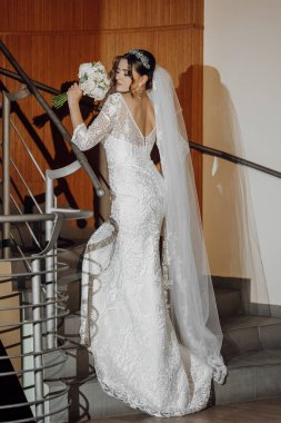 Gelinlik giymiş bir kadın merdivende elinde bir buket çiçekle dikiliyor. Gelin güzel bir elbise giyip elinde bir buket çiçek tutarken, zarafet ve kutlama kavramı.