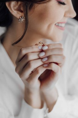 Bir kadın elinde bir yüzük tutuyor ve gülümsüyor. Mutluluk ve neşe kavramı, çünkü kadın yüzük için heyecanlı. Yüzüğün kendisi aşkın ve bağlılığın sembolüdür.