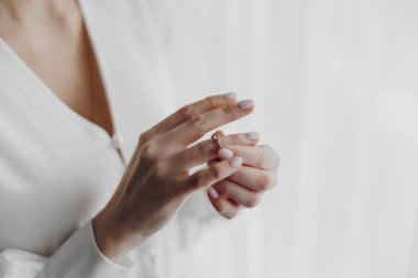 Bir kadın elinde bir yüzük tutuyor. Kadın beyaz bir elbise giyiyor.