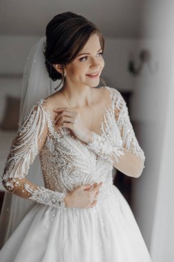 Gelinlikli bir kadın pencerenin önünde duruyor. Gülümsüyor ve pencereden dışarı bakıyor.