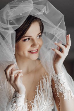 Duvak takan ve parmağında yüzük olan bir kadın. Gülümsüyor ve kameraya bakıyor.