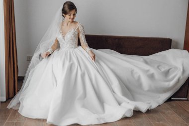 Beyaz gelinlikli bir kadın kanepede oturuyor. Elbise uzun ve dalgalı ve kadın peçe takıyor. Zarafet ve kutlama kavramı