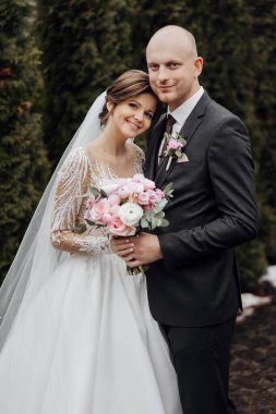 Bir gelin ve damat çiçekli bir resim için poz veriyorlar. Gelin beyaz bir elbise giyiyor ve damat da takım elbise giyiyor.