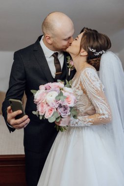 Bir adam ve bir kadın kameranın önünde öpüşüyorlar. Adamın elinde cep telefonu var.