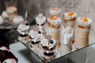 Plastik bardaklarda çeşitli tatlılar bulunan bir masa, bazıları yaban mersini ve ahududu içeriyor.