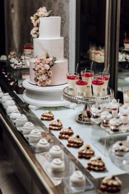 İçinde beyaz pasta ve bir sürü tatlı olan bir masa. Tatlılar öyle bir düzenlenmiş ki, yenmeye hazırmış gibi görünüyorlar. Sahne kutlama ve davetkar.