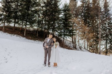 Karda bir çift var, gelin elinde buket tutuyor. Sahne arka planda ağaçlar olan bir ormanda geçiyor. Sahne romantik ve sakin.