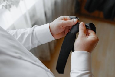 Bir adam siyah bir kravat tutuyor ve ayarlıyor. Formalite kavramı ve detaylara dikkat, çünkü adam kravatını düzgün bir şekilde hizalamak için dikkatlice ayarlıyor.