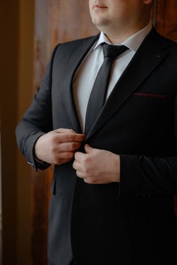 Takım elbiseli bir adam kravatını bağlamaya hazırlanıyor. O siyah bir takım ve beyaz bir gömlek giyiyor.