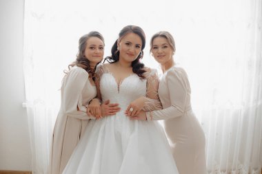 Üç kadın pencerenin önünde poz veriyor. Hepsi beyaz elbiseler giyiyor ve gülümsüyorlar. Sahne mutlu ve dostane.