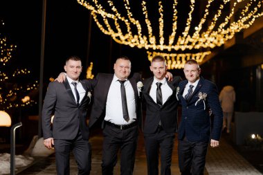 Takım elbiseli dört adam ışıklı bir tabelanın altında fotoğraf için poz veriyor. Sahne, erkekler takım elbise ve kravat giydiği için kutlama ve resmi.