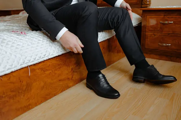 stock image A man in a suit is sitting on a bed with his feet up. He is wearing black dress shoes and is adjusting them. Concept of relaxation and comfort, as the man is taking a break from his formal attire