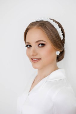 İnci bantlı ve küpeli bir kadın kameraya gülümsüyor. Kadın beyaz gömlek ve inci aksesuar giydiği için zarafet ve incelik kavramı.