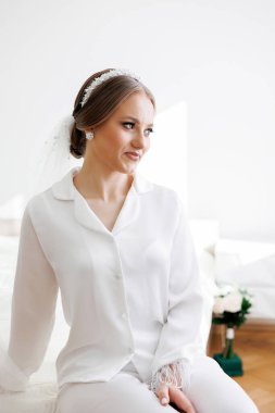 Beyaz pijama takımlı bir kadın yatağa oturur. Beyaz bir saç bandı takıyor ve saçları topuz şeklinde.