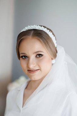 İnci bantlı bir kadın kameraya gülümsüyor. Görüntünün sıcak ve davetkar bir havası var. Kadının gülüşü ve elbisesinin yumuşak, beyaz rengi.