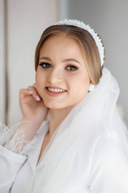 Beyaz peçeli ve boncuklu bantlı bir kadın gülümsüyor. Beyaz bir elbise ve beyaz bir gömlek giyiyor.