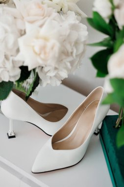 Bir vazo çiçeğin yanındaki masada bir çift yüksek topuklu ayakkabı sergilenir. Ayakkabılar sivri ve zarif, ve çiçekler sahneye tazelik ve renk katıyor.