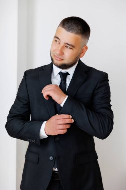 Takım elbiseli bir adam kravatını bağlamaya hazırlanıyor. O siyah bir takım ve beyaz bir gömlek giyiyor.