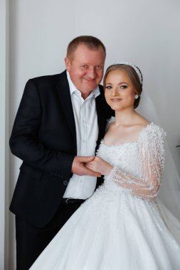 Bir adam ve bir kadın resim için poz veriyorlar. Adam takım elbise giyiyor ve kadın da gelinlik giyiyor. Sahne mutlu ve kutlama dolu.